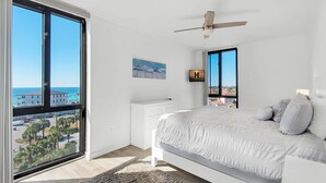 A bedroom with a large window, a bed, a ceiling fan, and a view of the ocean. - Enclave 702A | 7th Floor Penthouse • Across from Gated Beach • Pool-View Balcony (Destin)
