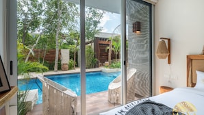 A modern hotel room with a sliding glass door leading to a private pool area, a bed with a white headboard, and a small wooden nightstand. - NHOA 107B Lux 1BR Condo Pool access in Aldea Zama (Tulum)