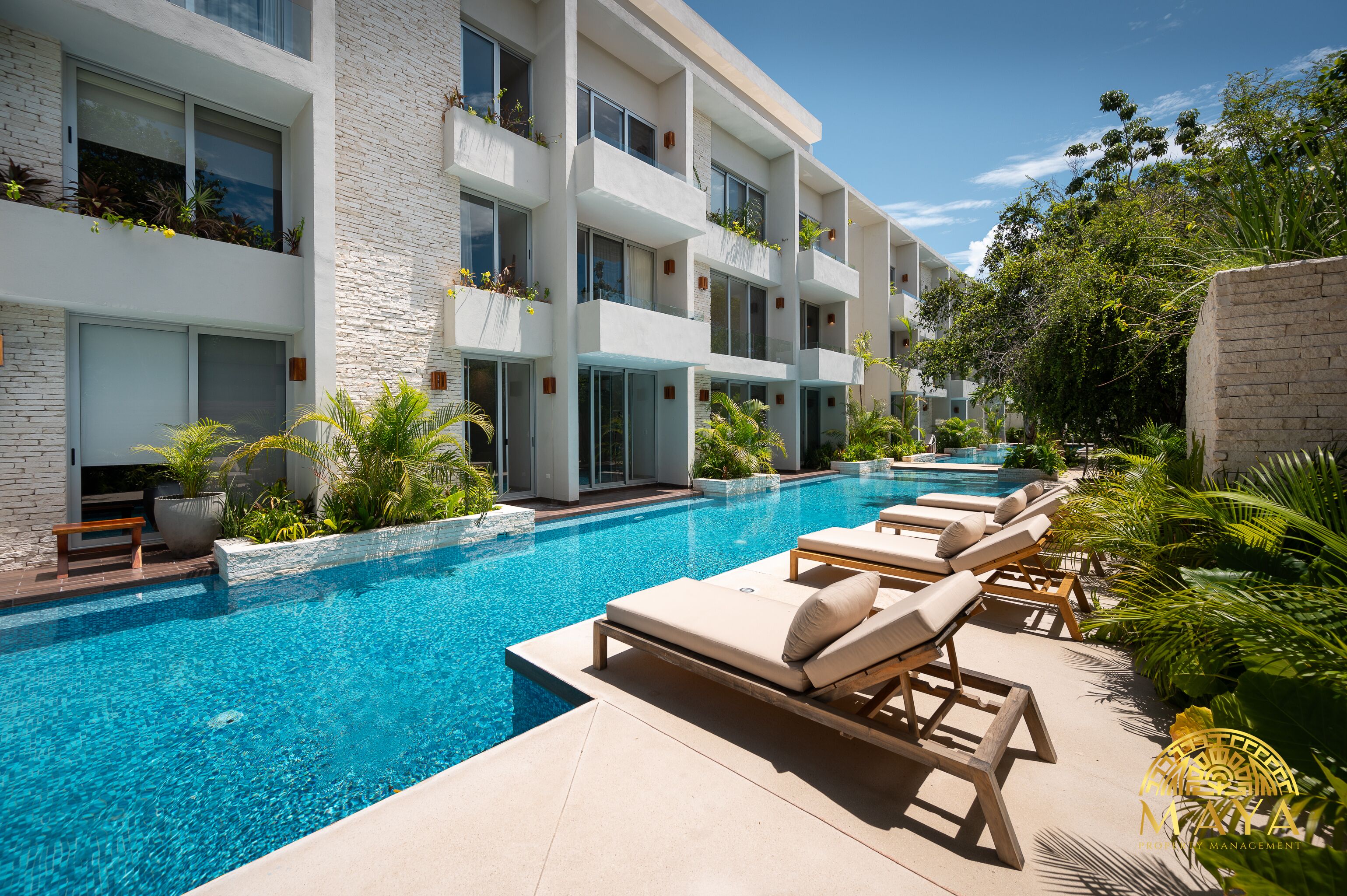 A modern hotel with a swimming pool, lounge chairs, and potted plants.