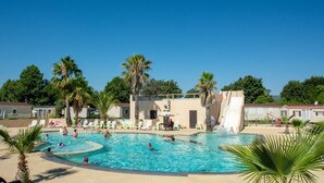 Zona de piscina con varias piscinas, sillas de descanso, palmeras y un tobogán.