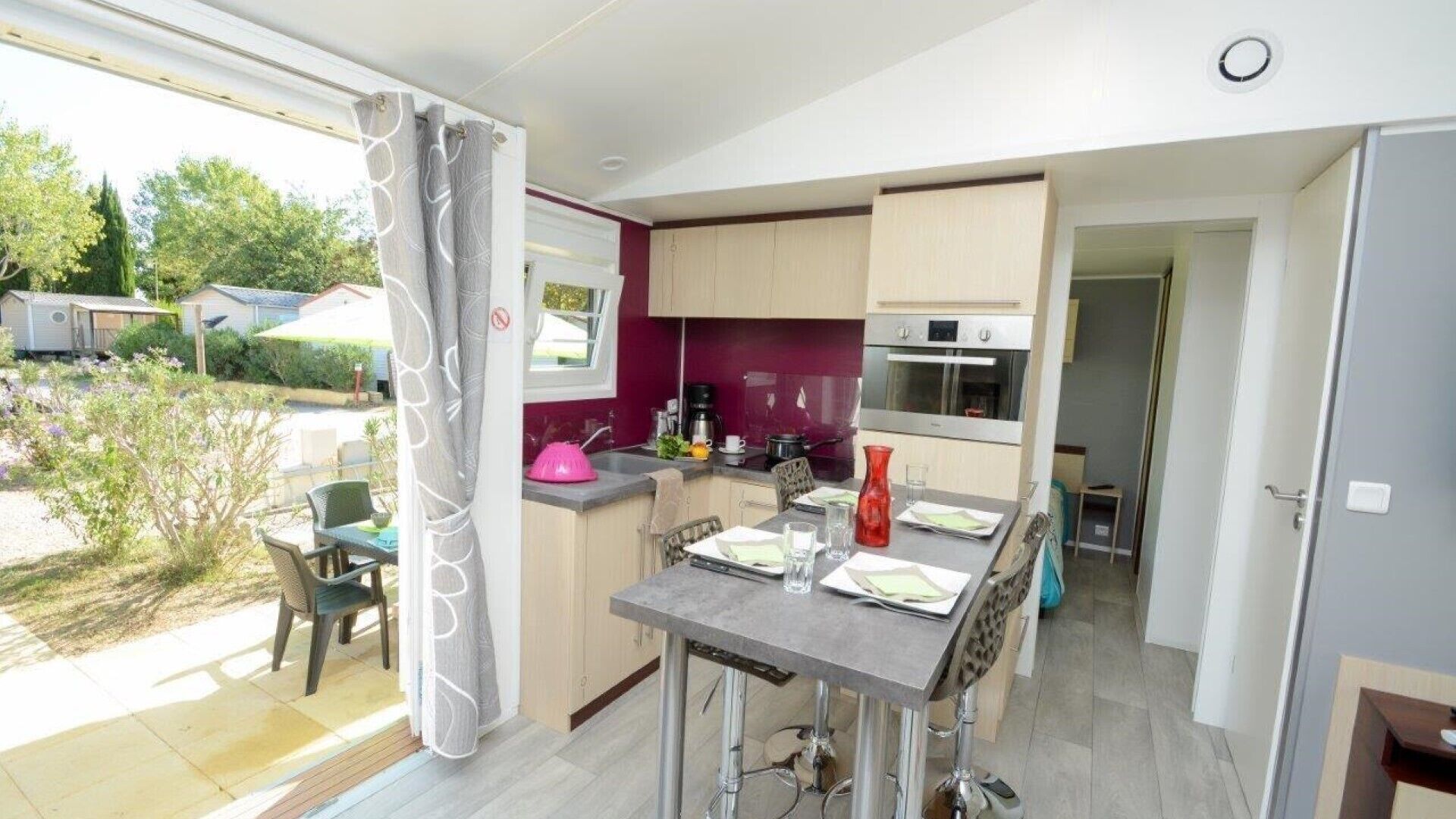 A compact kitchen with a dining area, a large window with curtains, and a view of the outside.