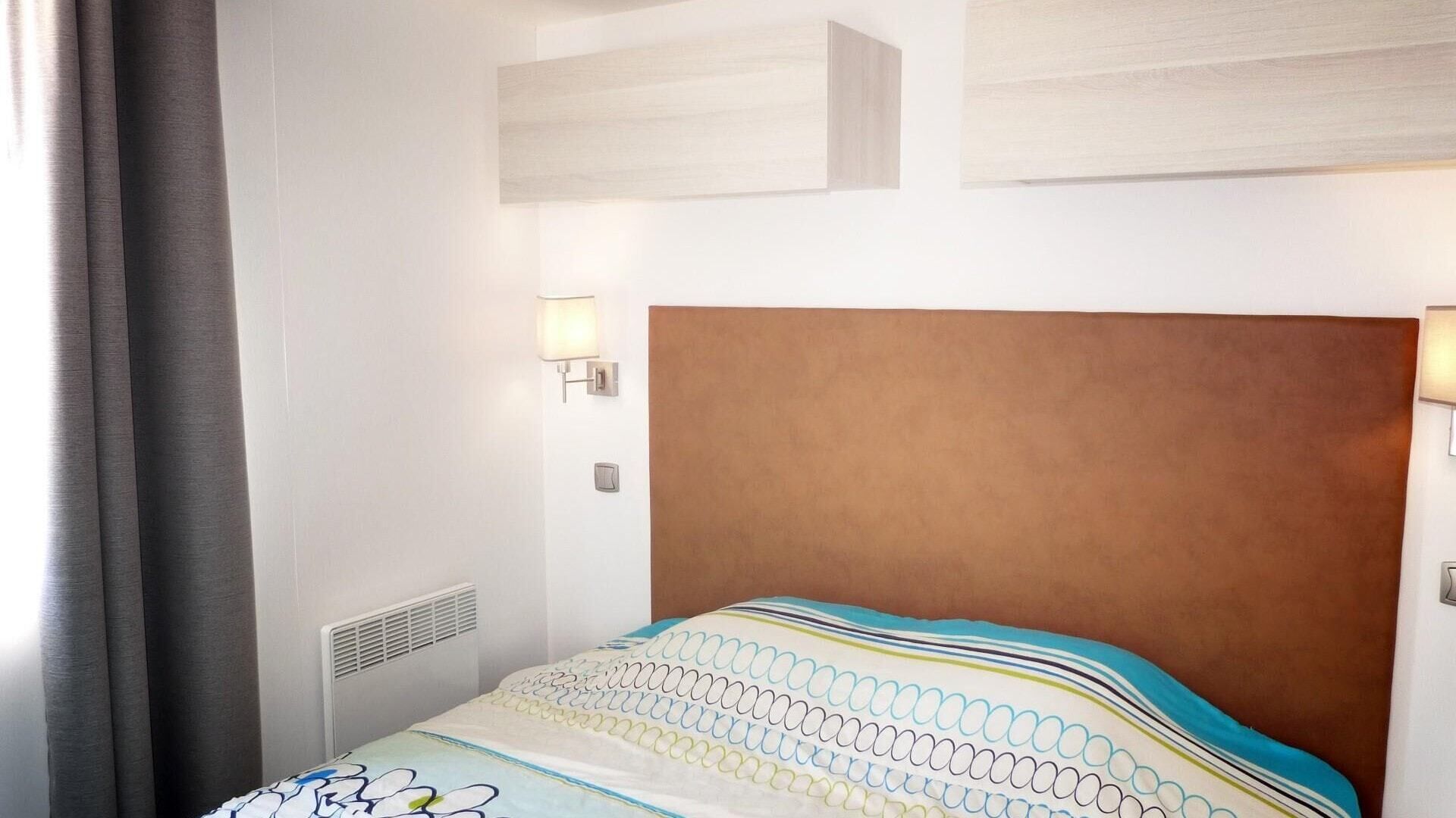 A hotel room with a large bed, a headboard, two wall-mounted lights, and a vent.