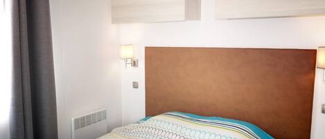A hotel room with a large bed, a headboard, two wall-mounted lights, and a vent.