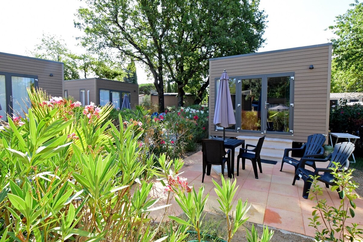 A modern outdoor patio area with a table and chairs, surrounded by lush greenery and flowering plants.