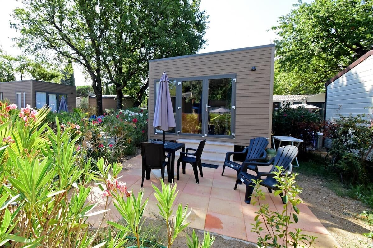 Ein moderner Außenbereich mit Terrasse, Tisch und Stühlen, umgeben von üppigem Grün und blühenden Pflanzen.