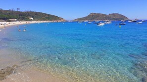 Una playa con agua cristalina, barcos y gente.
