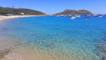 Una playa con agua cristalina, barcos y gente.
