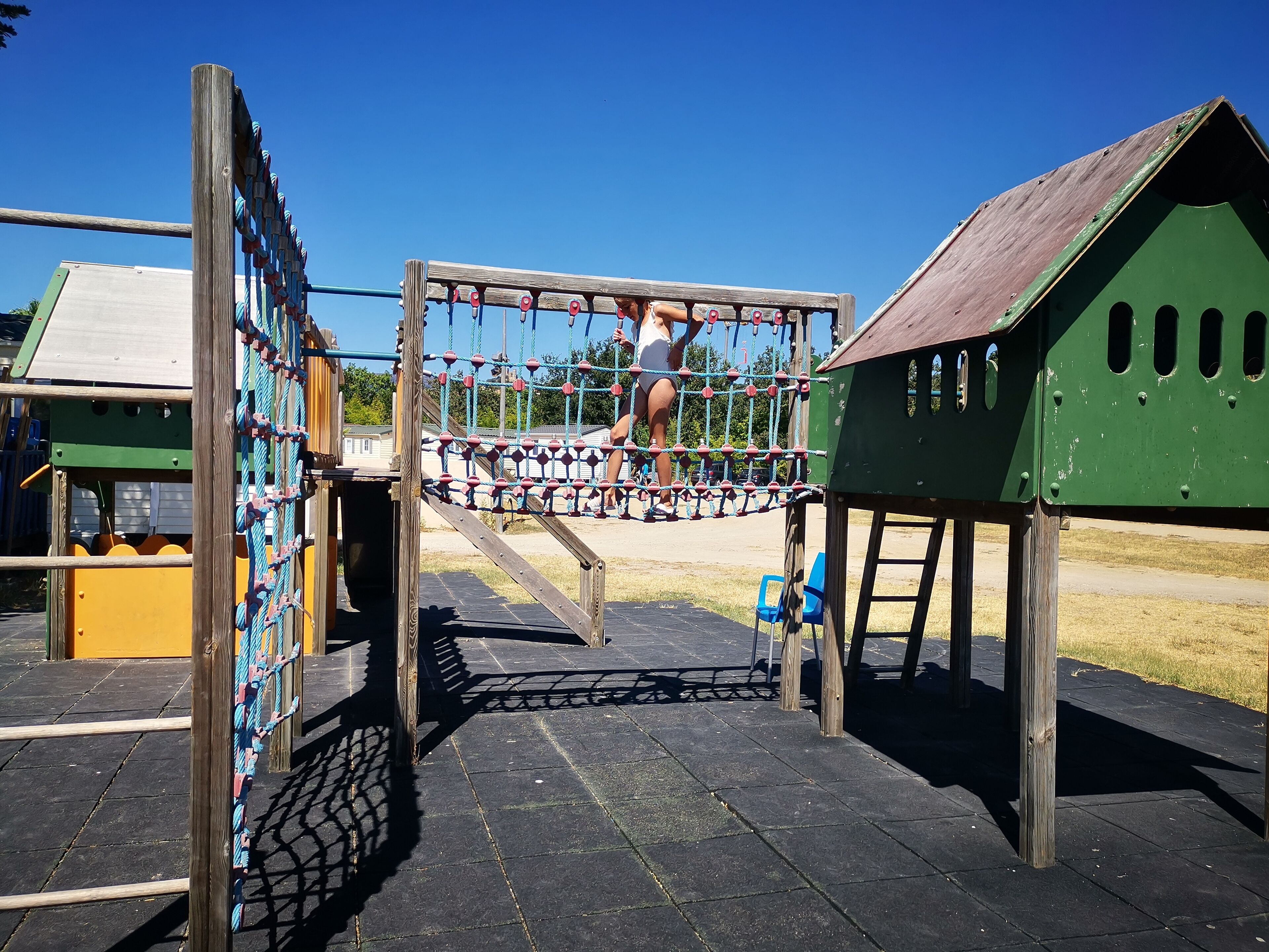 Un parque infantil con un puente de cuerda, una estructura para escalar y un pequeño refugio verde.