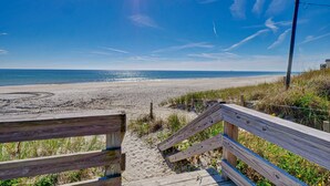 A wooden boardwalk leading to a sandy beach with a clear blue sky and ocean view.