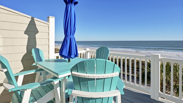 A deck with a table and chairs, overlooking the ocean.