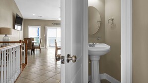 A hotel room with a white door, a pedestal sink, a flat-screen TV mounted on the wall, and a dining area with a table and chairs.