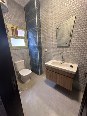 Bathroom features a toilet, sink, and shower area with a tiled wall.