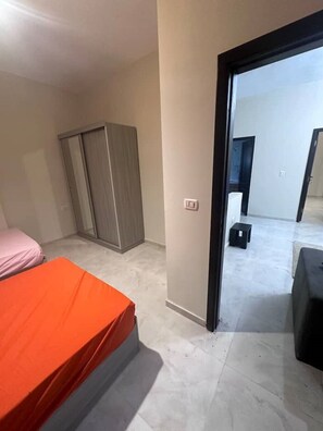 Cozy retreat with a comfortable bed, wardrobe, and small table, set against a tiled floor.