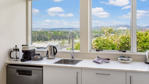 A kitchen with a large window, a coffee maker, a kettle, and a dish rack. - Serene Breeze Escape with estuary view (Whitford)