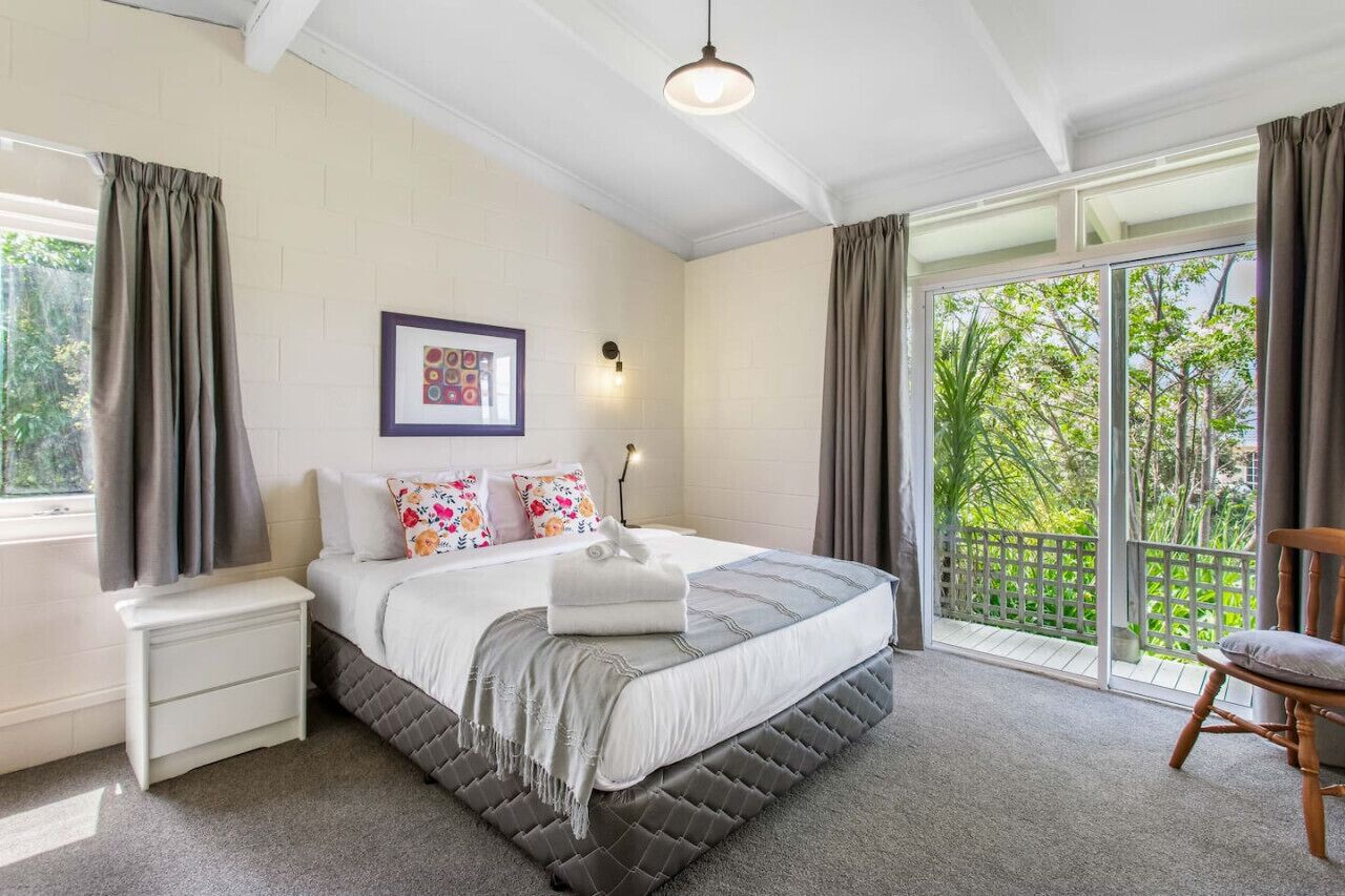 Un dormitorio con una cama grande, una mesita de noche, cortinas y vistas al exterior.