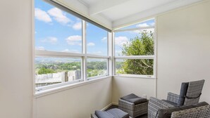 A corner room with large windows offering a view of greenery and distant landscape. There are wicker sofas and a small table. - Serene Breeze Escape with estuary view (Whitford)