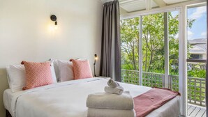 A hotel room with a large bed, a nightstand with a lamp, and a view of greenery through the window. - Serene Breeze Escape with estuary view (Whitford)