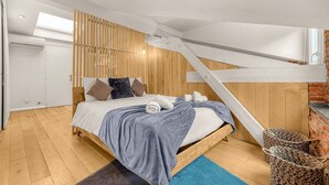 Ein Schlafzimmer mit einem hölzernen Bett, einer geneigten Decke und Blick auf eine Ziegelwand.