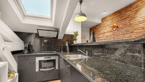 Eine moderne Küche mit dunklen Schränken, einer Granit Arbeitsplatte, einem Oberlicht und einer Wand mit Backsteinverkleidung.