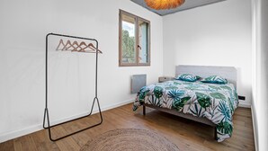 Ein Schlafzimmer mit einem Bett, einer Pendelleuchte, einem Fenster und Holzboden.
