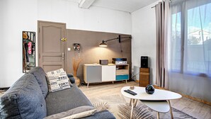 Ein modernes Wohnzimmer mit einem grauen Sofa, einem kleinen weißen Tisch und einer Holzkassette mit einem Flachbildfernseher.
