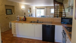 A compact kitchen with a dishwasher, a microwave, a sink, and a wooden staircase leading to an upper level.