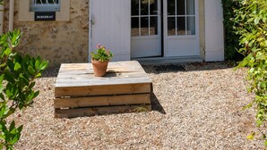 A rustic building with a tiled roof, a wooden bench with a potted plant, and a sign reading "BERGERAC".