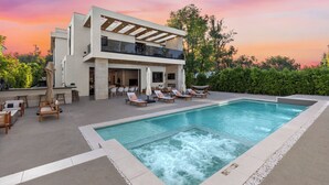 Une maison moderne à deux étages dotée d’une piscine, d’un espace salon extérieur et d’un patio.