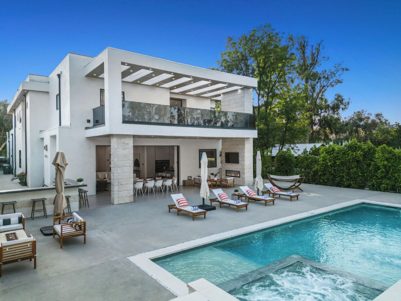 A modern two-story house with a swimming pool, outdoor seating, and a patio area.