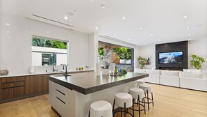 Une cuisine moderne dotée d’un îlot central, de tabourets de bar, d’un grand téléviseur et d’un coin salon avec un canapé.
