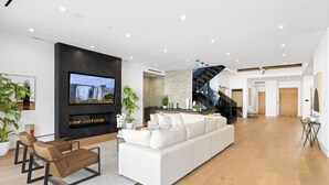 Un salon moderne doté d’un grand téléviseur à écran plat, d’une cheminée, d’un canapé blanc et d’un escalier menant à un niveau supérieur.