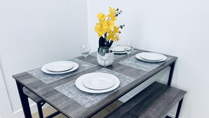 Ein Esstisch mit vier weißen Tellern, zwei Weingläsern und einer Vase mit gelben Blumen.