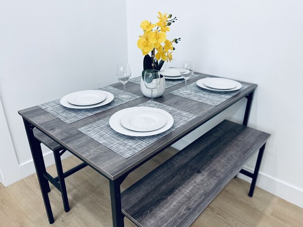 Una mesa de comedor con cuatro platos blancos, dos copas de vino y un jarrón con flores amarillas.