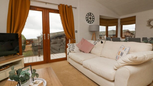 A living room with a sofa, a coffee table with a plant, a TV, and a sliding glass door leading to a balcony. - Serenity Sunset (Ilfracombe)