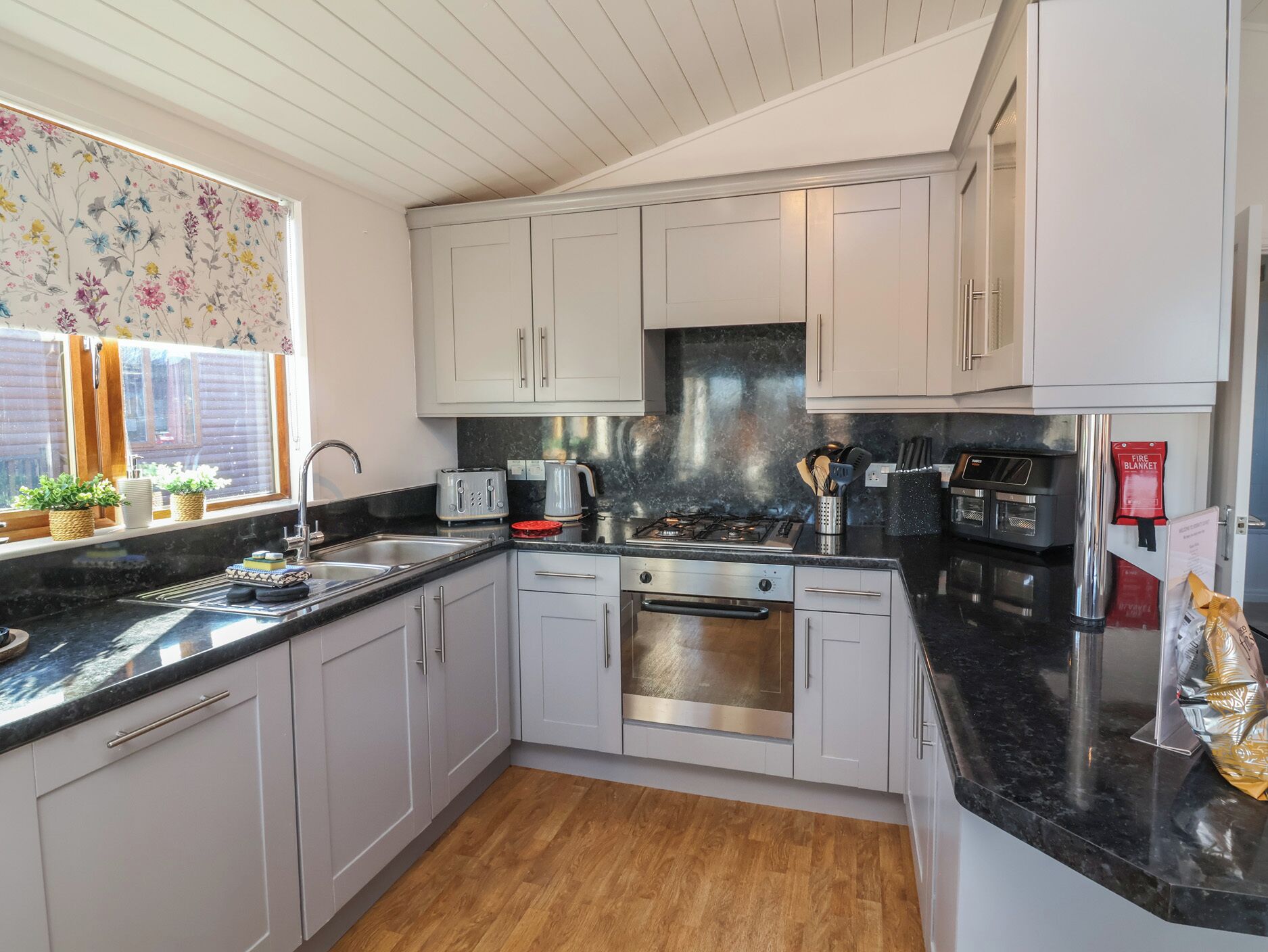 A modern kitchen with white cabinets, a black countertop, stainless steel appliances, and a window with a floral curtain.