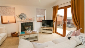A living room with a sofa, a TV, a fireplace, and a window with curtains. - Serenity Sunset (Ilfracombe)