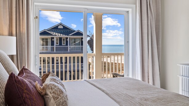 Een slaapkamer met een bed, uitzicht op een strand en een gebouw door een glazen deur.
