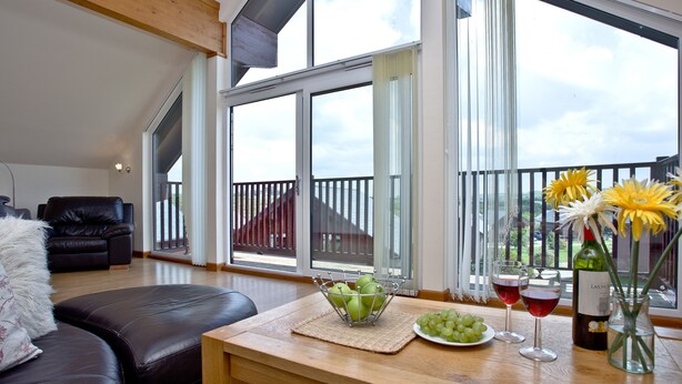 A spacious room with a leather sofa, a wooden table with a bowl of fruit, wine glasses, and a bottle of wine.
