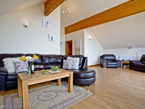 A modern living room with a leather sofa, a wooden coffee table, and a patterned rug. - Cedar Lodge - Retallack (St Columb)