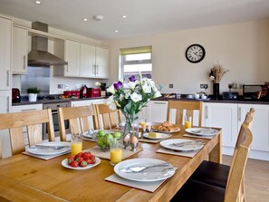 Una cocina moderna con armarios blancos, una campana extractora de acero inoxidable, una mesa de comedor dispuesta con platos, vasos y un jarrón de flores.