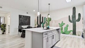 Una cucina moderna con isola centrale, luci a sospensione e un murale a tema cactus.
