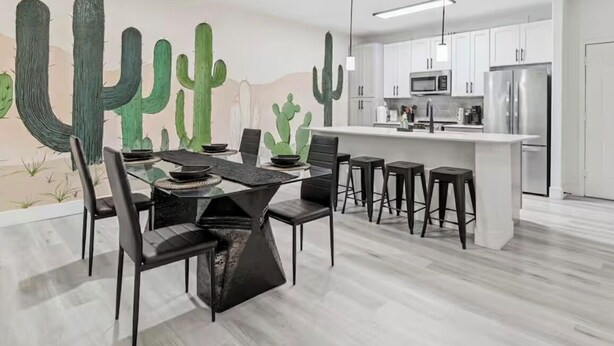 Una cucina moderna con mobili bianchi, un'isola centrale e un'area pranzo con tavolo in vetro e sedie nere.