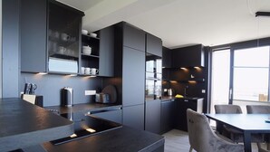 A modern kitchen with dark cabinetry, a central island, and a dining area with chairs.