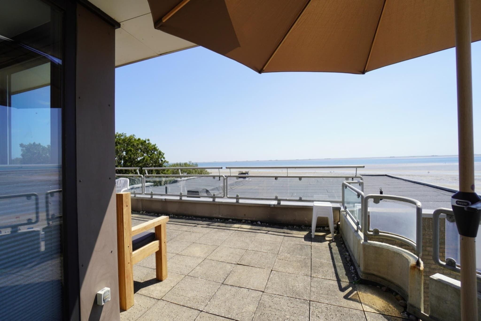 Un balcon avec vue sur la mer, une chaise en bois et une rambarde en métal.