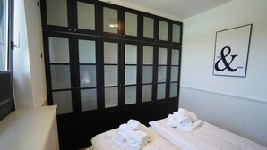 Ein Hotelzimmer mit zwei Betten, einem großen Schrank mit satinierten Glaselementen und einem an der Wand befestigten Schild mit '&'.