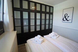 Ein Hotelzimmer mit zwei Betten, einem großen Schrank mit satinierten Glaselementen und einem an der Wand befestigten Schild mit '&'.