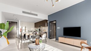 A modern living room with a sofa, coffee table, and TV. There is a kitchen in the background with cabinets and a fridge.