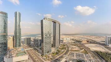 A modern high-rise building with a curved top, surrounded by other tall buildings and a coastal view.
