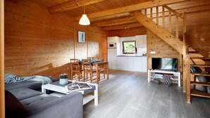 L’intérieur d’un chalet en bois chaleureux et accueillant, avec un coin repas, un canapé, un téléviseur et un escalier.