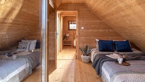 Une chambre mansardée avec des murs en bois et un plafond en pente, comprenant deux lits, une petite fenêtre et une plante en pot.